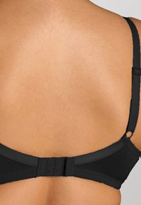 Reggiseno nero con spalline regolabili, tessuto liscio e chiusura con ganci dietro. Presenta un design senza cuciture.