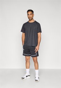 Μαύρο αθλητικό t-shirt με κοντά μανίκια και υφασμένη υφή. Συνδυασμένο με μαύρο σορτς από δίχτυ με λευκή επένδυση και μαύρα/λευκά αθλητικά παπούτσια.