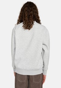Sudadera gris claro con un ajuste relajado, puños acanalados y dobladillo. Textura suave con un diseño liso, vista desde la parte de atrás. Pantalones marrones visibles.