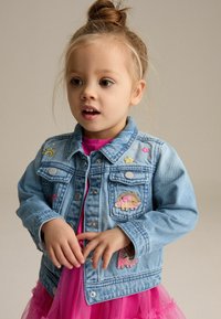 Hellblaues Jeansjacke mit gestickten Motiven von einer Sonne, Blumen und Tieren. Abgeschlossen mit silbernen Knöpfen und einem klassischen Kragen.