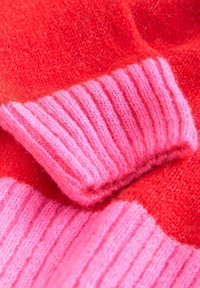 Kötött pulóver élénk piros és rózsaszín színvilággal. Rózsaszín bordás gallérral és sima textúrával rendelkezik, kiemelve a kontrasztos árnyalatokat.