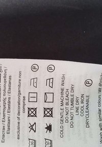Étiquette d'entretien avec des symboles de lavage sur un fond de tissu clair, présentant des instructions de lavage, de repassage et de séchage tracées en noir.