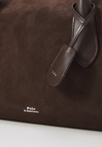 Krupni plan smeđe suede torbe s kožnim detaljima i oznakom s utisnutim natpisom "Polo by Ralph Lauren" u bijeloj boji.