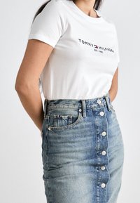 Vit bomull T-shirt med "TOMMY HILFIGER" logotyp. Ljust blå denimkjol med framknappar, medellång, med en ficka som har en färgad rand som accent.
