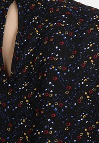 Tessuto floreale nero con piccoli fiori rossi, blu e gialli; presenta un'apertura a chiave sul retro; texture morbida.