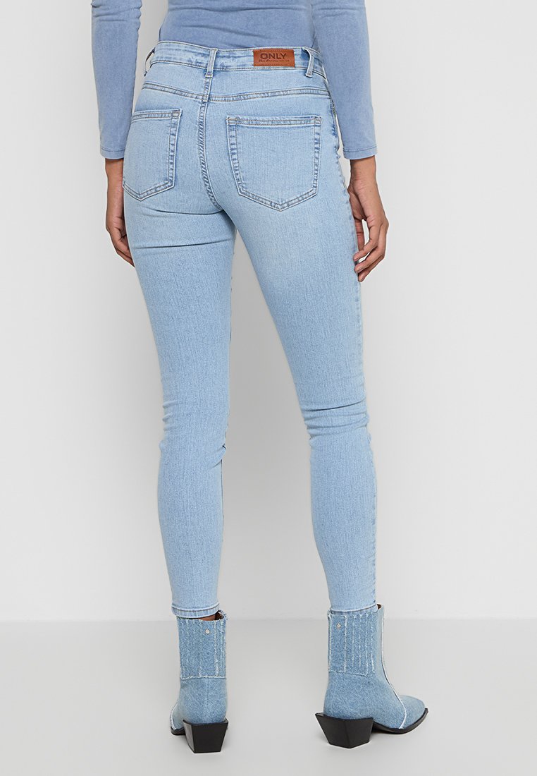 Helle blaue, hoch taillierte Skinny-Jeans mit einer glatten Denim-Oberfläche, ausgestattet mit Gesäßtaschen und einem Lederlabel. Kombiniert mit Denim-Absatzstiefeln.