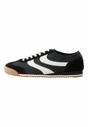 Black and white low-top sneaker with white laces, tan rubber sole, and zigzag tread pattern on the outsole.
