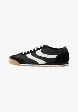 Schwarz-weißer Low-Top-Sneaker mit weißen Schnürsenkeln, beige-gummisohle und Zickzack-Profil auf der Laufsohle.