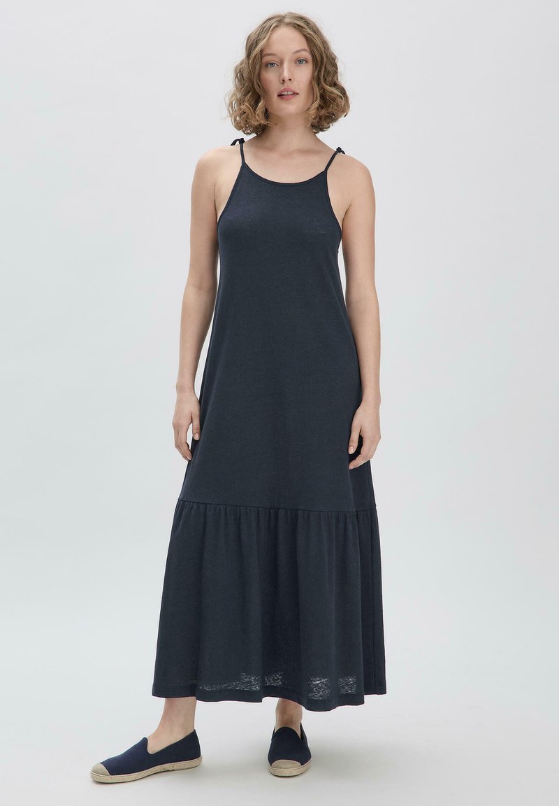 Dunkelgraues ärmelloses Maxikleid aus weichem Stoff, mit einem gestuften Saum und verstellbaren Bindebändern, kombiniert mit marineblauen Slippern.
