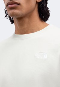 Gros plan d'une personne portant un t-shirt blanc à col rond avec le logo The North Face brodé sur la poitrine.