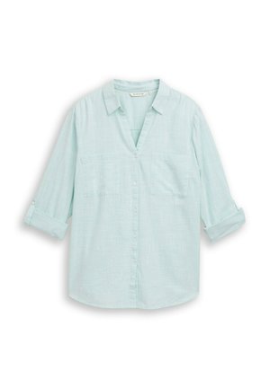 Jasnoniebieska, zapinana na guziki koszula z długim rękawem z podwiniętymi mankietami, dwoma kieszeniami na piersi i klasycznym kołnierzem, rozłożona płasko na białym tle.