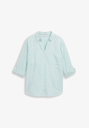 Lichtblauw overhemd met lange mouwen, opgerolde manchetten, twee borstzakken en een klassieke kraag, plat gelegd op een witte achtergrond.