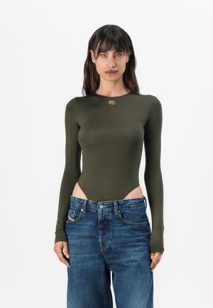 Langärmeliger, olivgrüner Bodysuit mit seitlichen Ausschnitten und rundem Ausschnitt, kombiniert mit lockeren blauen Jeans aus Denim. Glattes, dehnbares Material.