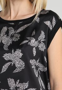 Black blouse with white floral pattern, short sleeves, round neckline, smooth texture, and a relaxed fit.