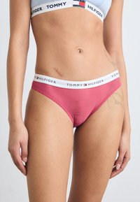 Rød og hvit stripete bikini-bunn med hvit elastisk midje som har "TOMMY HILFIGER"-logo. Mykt, elastisk materiale, lav høyde design.