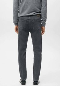 Pantalones vaqueros de mezclilla gris con un corte recto, dos bolsillos traseros y una textura sutil. Combinados con un suéter gris y zapatos negros visibles en la parte inferior.