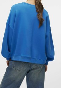 Sudadera azul de corte amplio con hombros caídos, textura suave, puños acanalados y dobladillo, combinada con jeans de denim de lavado medio.