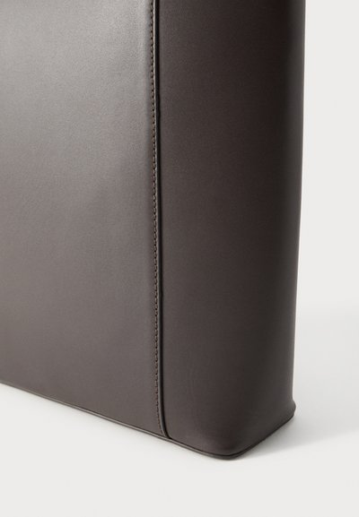 Κοντινό πλάνο γωνίας σκούρου καφέ δερμάτινης τσάντας με ορατή ραφή σε λευκό φόντο.