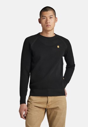 Black ribbed knit sweater with a crew neck, featuring a textured design, fitted cuffs, and a small gold logo on the chest.