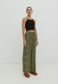 Schwarzes geripptes Cropped-Top kombiniert mit weit geschnittenen, grünen Leopardenmuster-Hosen mit elastischem Bund. Braune Clogs runden das Outfit ab.