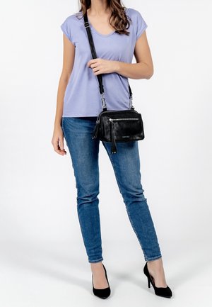 Czarna skórzana torba na ramię z srebrnymi zamkami błyskawicznymi, frędzlami i regulowanym paskiem, w połączeniu z lawendowym t-shirtem i niebieskimi dżinsami.