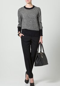 Pull gris et noir en maille avec un motif texturé, pantalon noir sur mesure, talons noirs et sac à main structuré noir.