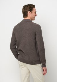 Suéter marrón de punto acanalado con cuello clásico, que presenta un ajuste holgado y una textura suave, mostrado desde la parte posterior sobre un fondo neutro.