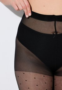 Schwarze, durchsichtige Strumpfhosen mit hohem Taillenbund. Sie besitzen einen glatten oberen Bereich und ein gepunktetes Muster im unteren Teil. Weiche, halbtransparente Textur.