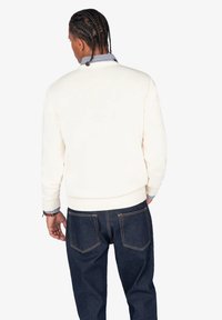 Suéter de punto color crema con puños y dobladillo acanalados, combinado con jeans de mezclilla azul oscuro que cuentan con dos bolsillos traseros y costuras en contraste.