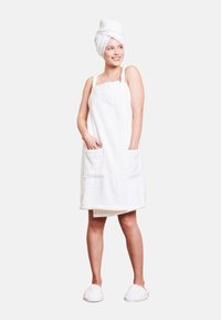 Accappatoio bianco e soffice con due tasche frontali e nastri regolabili, abbinato a una fascia bianca per i capelli e pantofole morbide.