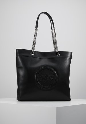 Czarna torba na ramię ze skóry z srebrnymi łańcuszkowymi uchwytami i wypukłym okrągłym logo przedstawiającym dwa ptaki na przodzie.