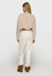 Langsleeve gestreepte top in beige en bruin, gecombineerd met crèmekleurige joggerbroeken. De schoenen zijn bruine suède laarzen met franjes.