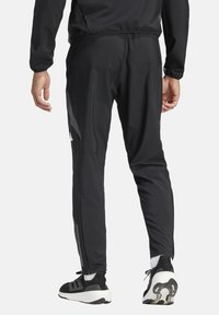 Schwarze Sporthosen mit schmalem Schnitt, leichtem Material, reflektierenden seitlichen Akzenten, Reißverschluss an den Knöcheln und kombiniert mit schwarz-weißen Sneakers.