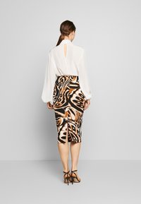 Blouse blanche à dos en keyhole, associée à une jupe noire ajustée avec un motif abstrait de papillons orange et marron et une fente à l'arrière.