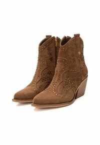 Botines de ante marrón con punta afilada, costuras decorativas y acentos de tachuelas. Cierre con cremallera y tacón apilado.