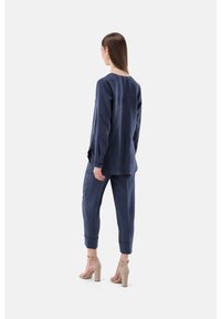 Marineblaue, lässige Bluse und Hose aus leichtem Stoff. Die Bluse hat einen runden Halsausschnitt; die Hose hat schmal zulaufende Beine mit Bündchen.