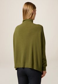 Zeleno-olivový oversized svetr s vysokým límcem, žebrovanými manžetami a lemem, vyrobený z měkké látky, zobrazený zezadu.