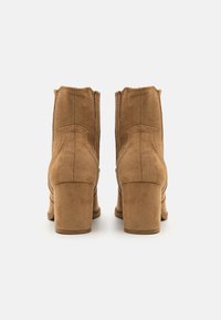 Brązowe zamszowe botki za kostkę z kwadratowym noskiem, zaokrąglonym tyłem i grubym obcasem. Posiadają delikatne przeszycia i gładką fakturę.