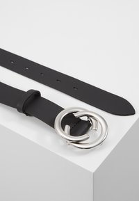 Zwarte leren riem met een brede band, voorzien van een ronde zilveren metalen gesp. Gladde textuur, minimalistisch ontwerp en meerdere verstelgaten.