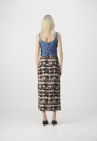 Denim crop top s priliehavým strihom, doplnený dlhou vzorovanou sukňou s abstraktnými čiernymi, béžovými a hnedými líniami. Čierne lodičky na opätku.