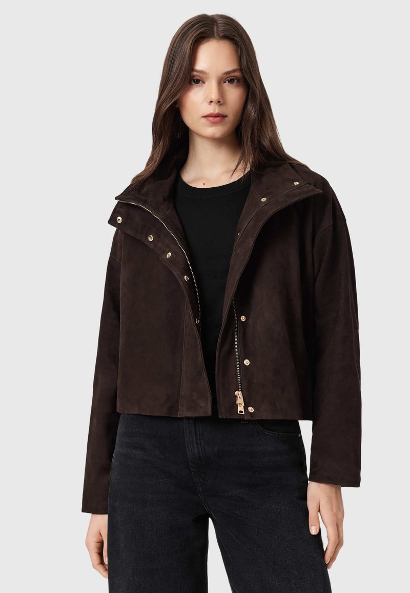 Giacca corta in camoscio marrone con collo alto, dettagli in oro, chiusura con zip e bottoni a pressione. Caratterizzata da una vestibilità rilassata e una texture morbida.