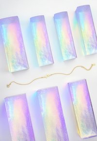 Bracciale d'oro con design a battito cardiaco su una catena, posizionato tra sei scatole iridescenti di colore viola con una texture glitterata.