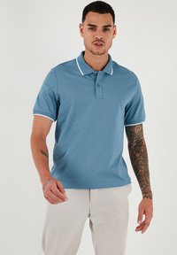 Polo tričko v světle modré barvě s bílým límcem a lemy rukávů. Krátké rukávy, zapínání na tři knoflíky a hladká, prodyšná tkanina.