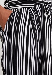 Tessuto a righe bianche e nere con un motivo a strisce larghe, dalla texture liscia e con un dettaglio di tasca laterale.