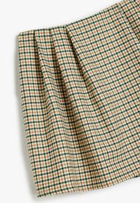 Plissé stof in een beige, groene en bruine ruitpatroon. Materiaal lijkt gestructureerd met een gelaagd ontwerp en scherpe randen.