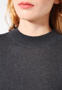 Maglione grigio scuro a maglia con scollo a coste. Il tessuto appare liscio e leggermente trasparente, con una vestibilità semplice e rilassata.