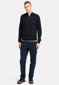 Navy quarter-zip sweater with ribbed cuffs and hem; layered over a cream shirt. Paired with dark blue pants and black and tan boots.