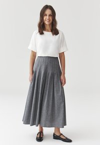 Crops top bianco con maniche arrotolate, abbinato a una lunga gonna plissettata grigia e scarpe nere con design T-strap.