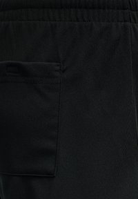 Zwarte joggingsbroek van zachte, gestructureerde stof. Voorzien van een elastische tailleband en een enkele achterzak met gestikte details.
