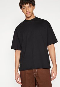 Sort oversized t-shirt lavet af bomuld, med korte ærmer og rund hals. Glat tekstur med en afslappet pasform og minimal detaljering.